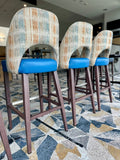 Three bar stools with patterned backrests and blue seats in a room with a geometric carpet.