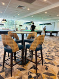 Bar stools around a pool table in a recreational area with people in the background.