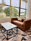 Brown leather sofa in a modern club lounge with large windows and a patterned rug.