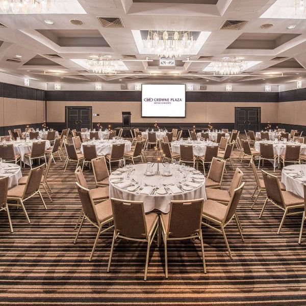 A function room in a hotel with tables and chairs set up for an event, with a presentation screen at the front.